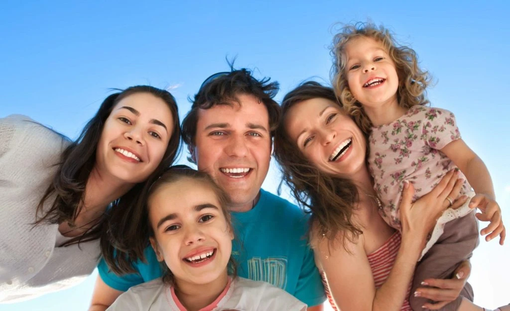 A smiling family together outdoors under a blue sky